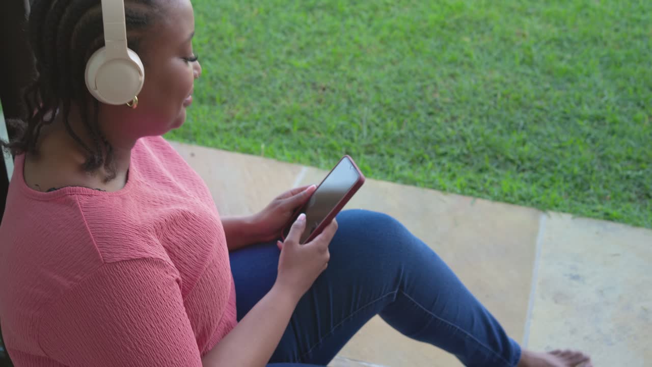 African American woman gazing at smartphone while sipping tea and tapping on patio, copy space
