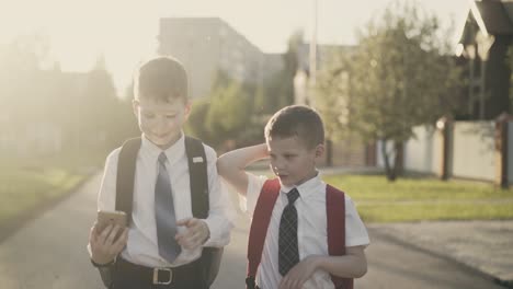 cu tracking two schoolchildren go home after school they talk hold a smartphone in their hands smile hug