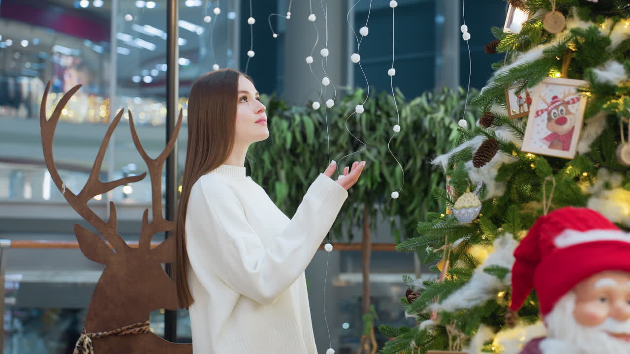 Lady standing and gently touching Christmas tree decorations, with illuminated festive ornaments and a Santa Claus figure in the background