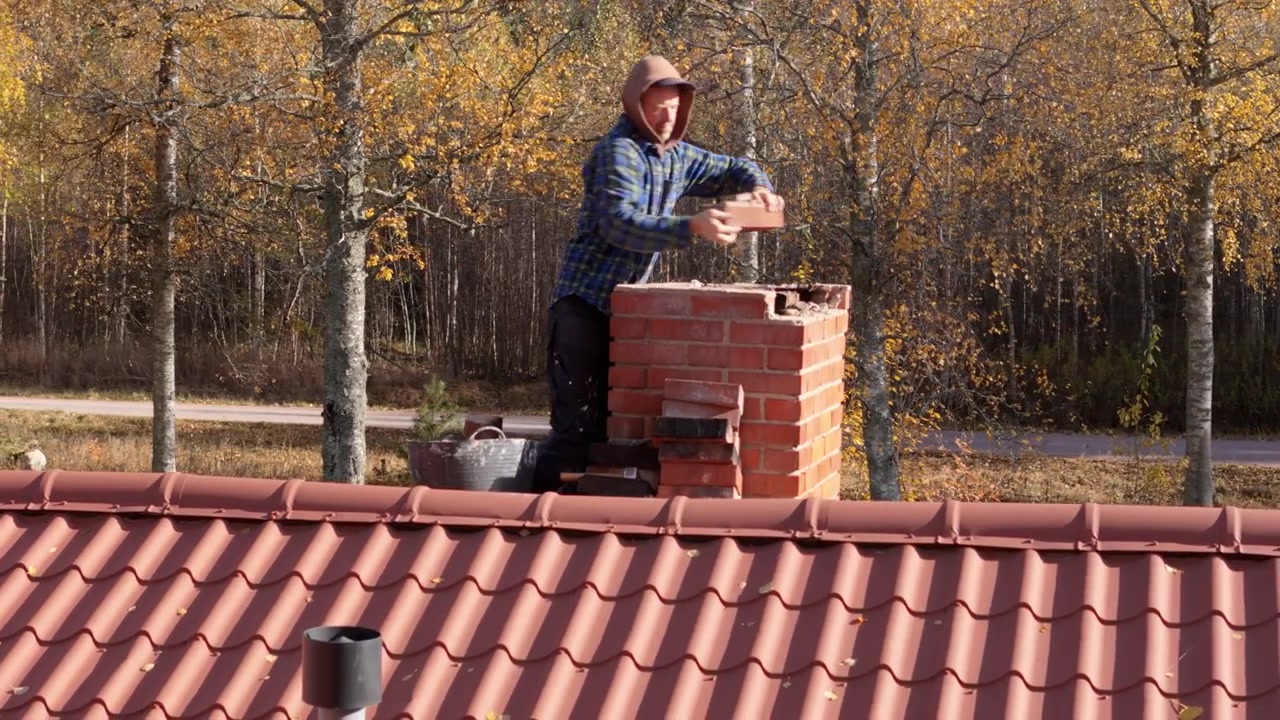 Brick chimney on red house rooftop being fixed by handyman, telephoto aerial