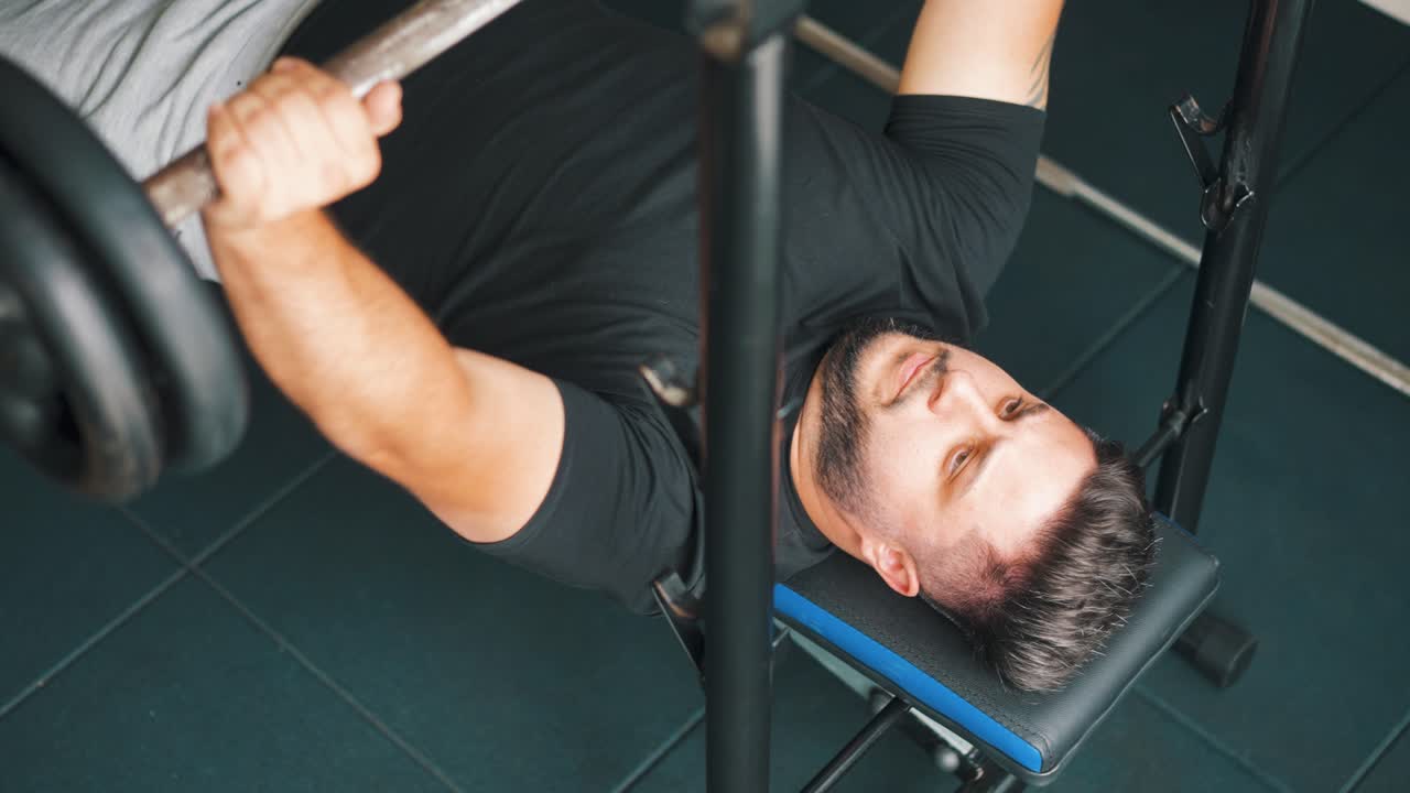 Pria muda perkasa berlatih angkat beban (bench press) di gym.