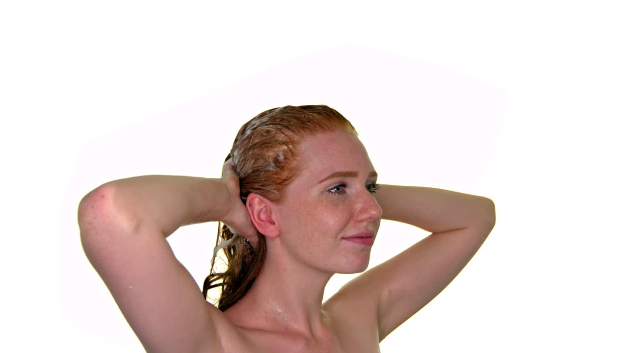 hermosa mujer atractiva aplicando champú en su cabello mientras masajea suavemente su cabeza mientras está dentro de un baño con fondo blanco aislado ideal para el cuidado del cabello simulado