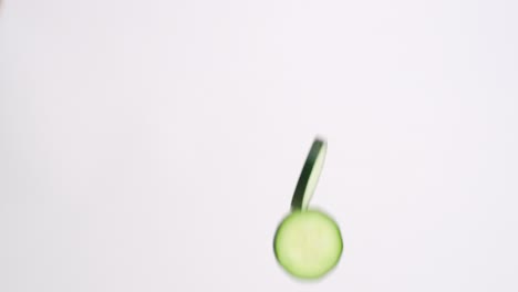 slow motion cucumber slices raining down on white backdrop