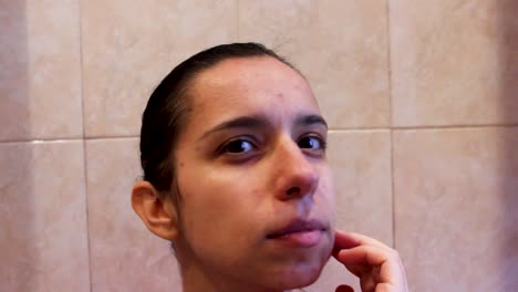 Young-woman-with-acne-observing-her-face-skin-in-bathroom,-close-up