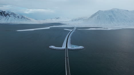 kolgrafarfjörður iceland establishing aerial shot of car traveling across bridge over glacial water, snowy mountains in background