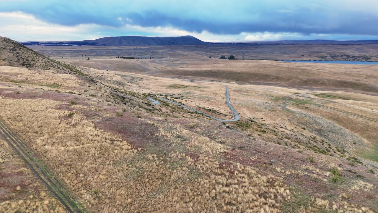 Flyover grassy ridge of rolling golden landscape under overcast sky