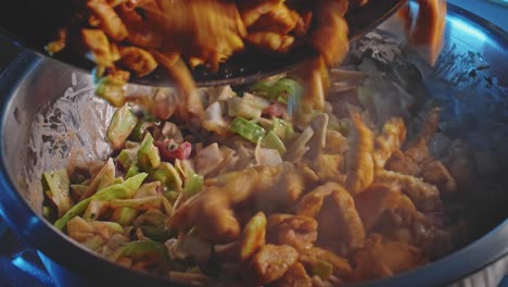 a close up of adding seasoned steaming cooked chicken breast pieces into a metal bowl that has chopped salad and vegetables then mixed thoroughly with a wooden spoon