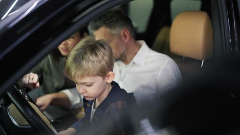 Close-up-of-a-little-blond-boy-in-a-plaid-shirt-sits-with-his-father-and-mother-in-the-interior-of-a-car-in-a-car-dealership