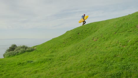 A-surfer-carries-his-board-up-a-hill-as-he-hikes-to-a-remote-surf-spot-in-a-coastal-area