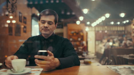 Junger-Mann-Benutzt-Telefon-Und-Trinkt-Kaffee-In-Einem-Café