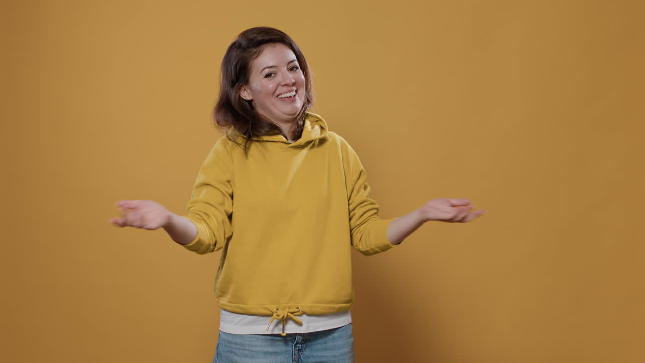 A young woman in a yellow hoodie smiling and shrugging