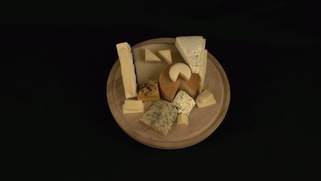 Round-board-with-mixed-hard-and-soft-cheese-rotate-on-black-background