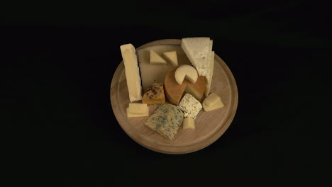 round board with mixed hard and soft cheese rotate on black background