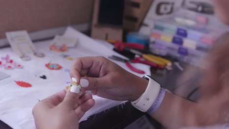 primer plano de las manos de la mujer haciendo artesanías con pequeñas cuentas coloridas, aguja e hilo 005