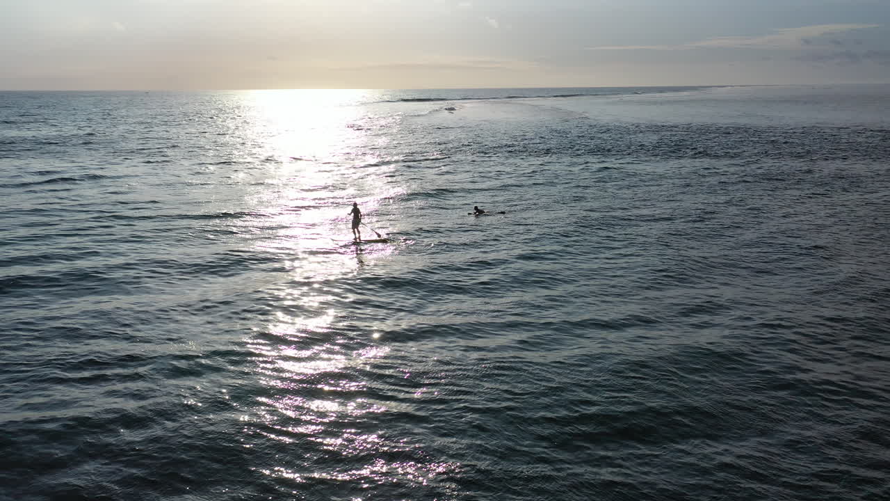 paddleboarder y un surfista disfrutando de las tranquilas aguas alrededor de la isla de la reunión mientras se pone el sol