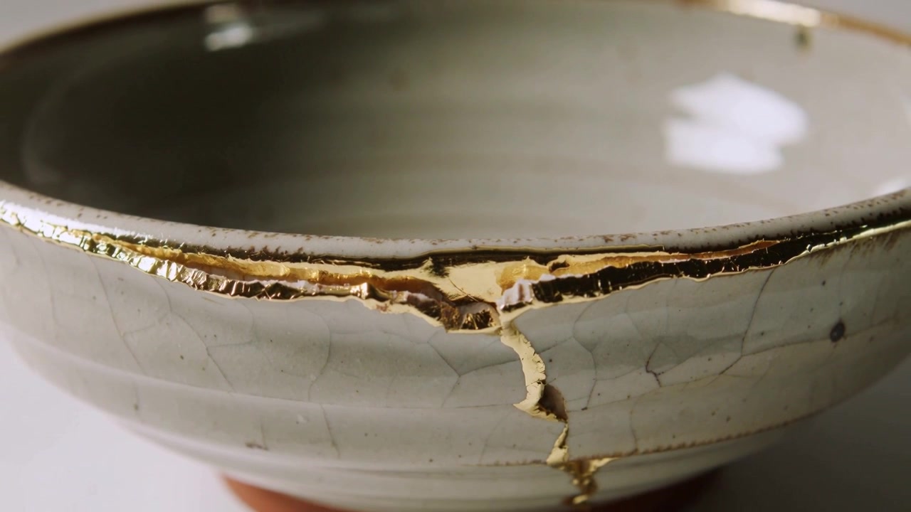 Câmera recuando, revelando tigela de celadon reparada sobre a mesa, mostrando incrustação de ouro para destacar o reparo.