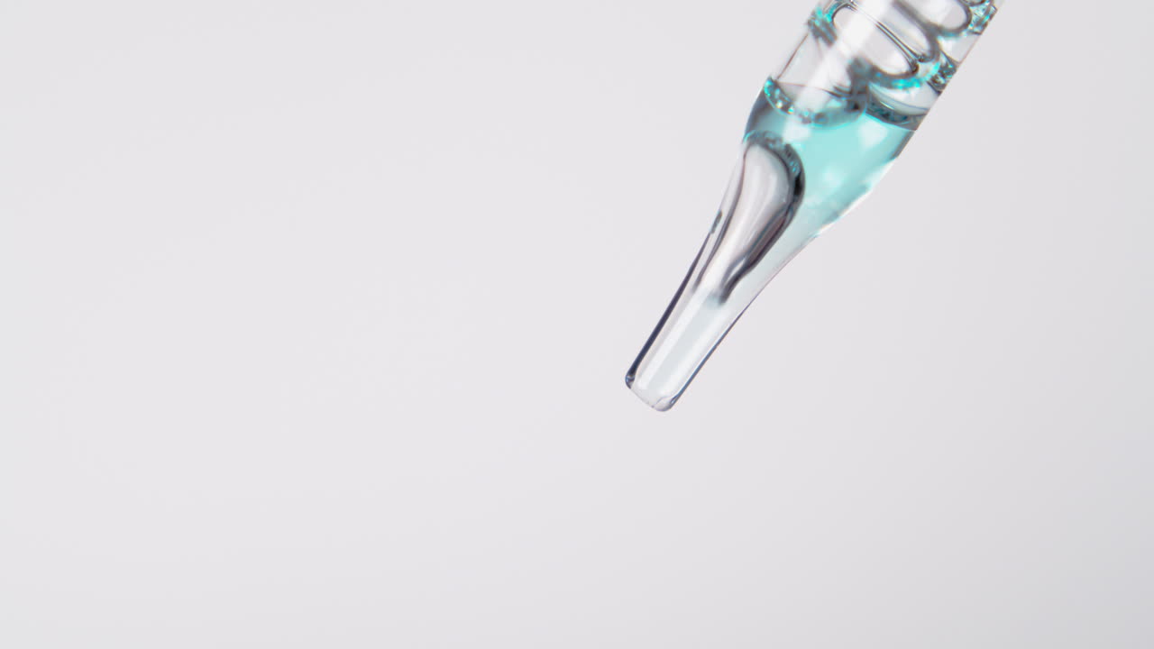 Drops of modern liquid falling down from glass pipette, isolated on white background