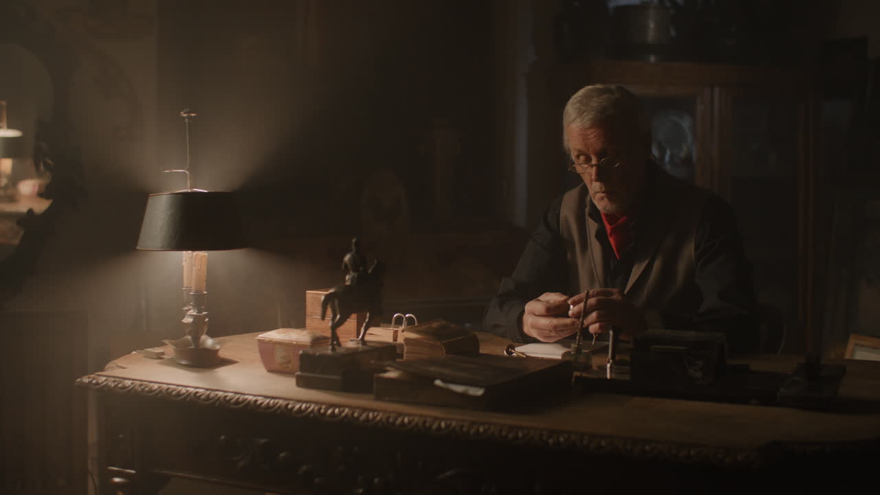 Older passionate man evaluates an old silver skull watch in his office at night