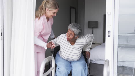 smiling caucasian nurse with senior african american woman patient in wheelchair, slow motion