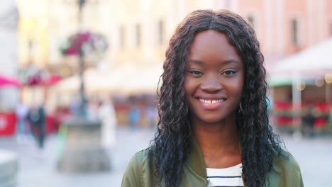 vista cercana de la mujer afroamericana con el pelo rizado mirando a la cámara y sonriendo en la calle