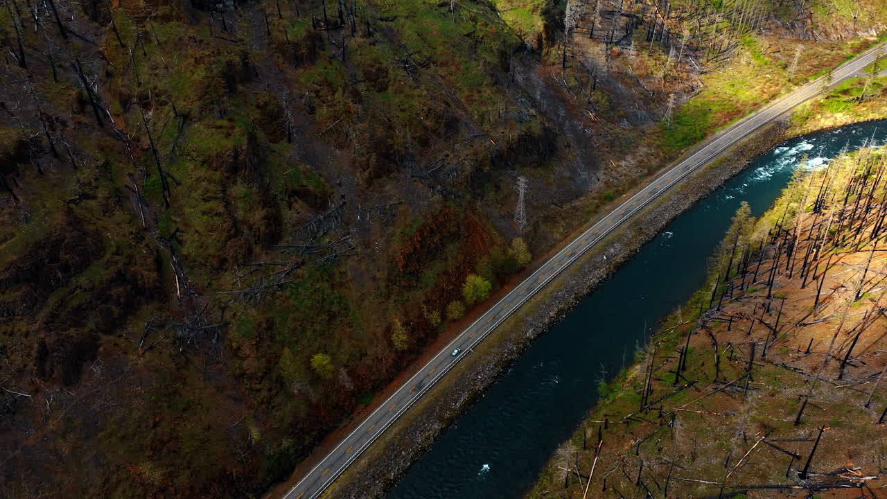 Beautiful blue narrow river flows along the highway at the foot of mountains. Top view on the car riding by the road.