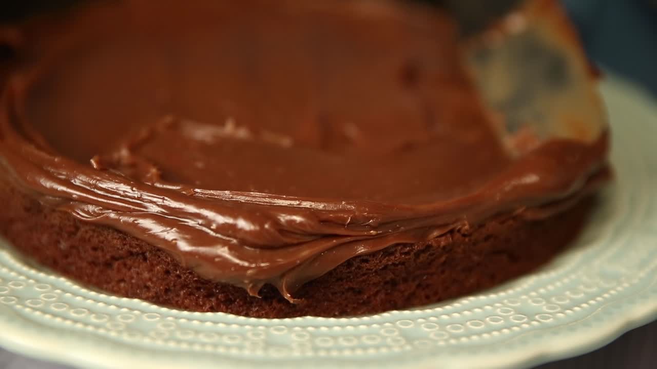Glaseando la primera capa de un pastel con cobertura de chocolate - primer plano aislado