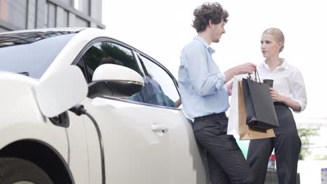 hombre de negocios y mujer de negocios progresistas apoyándose en el coche y el punto de carga.