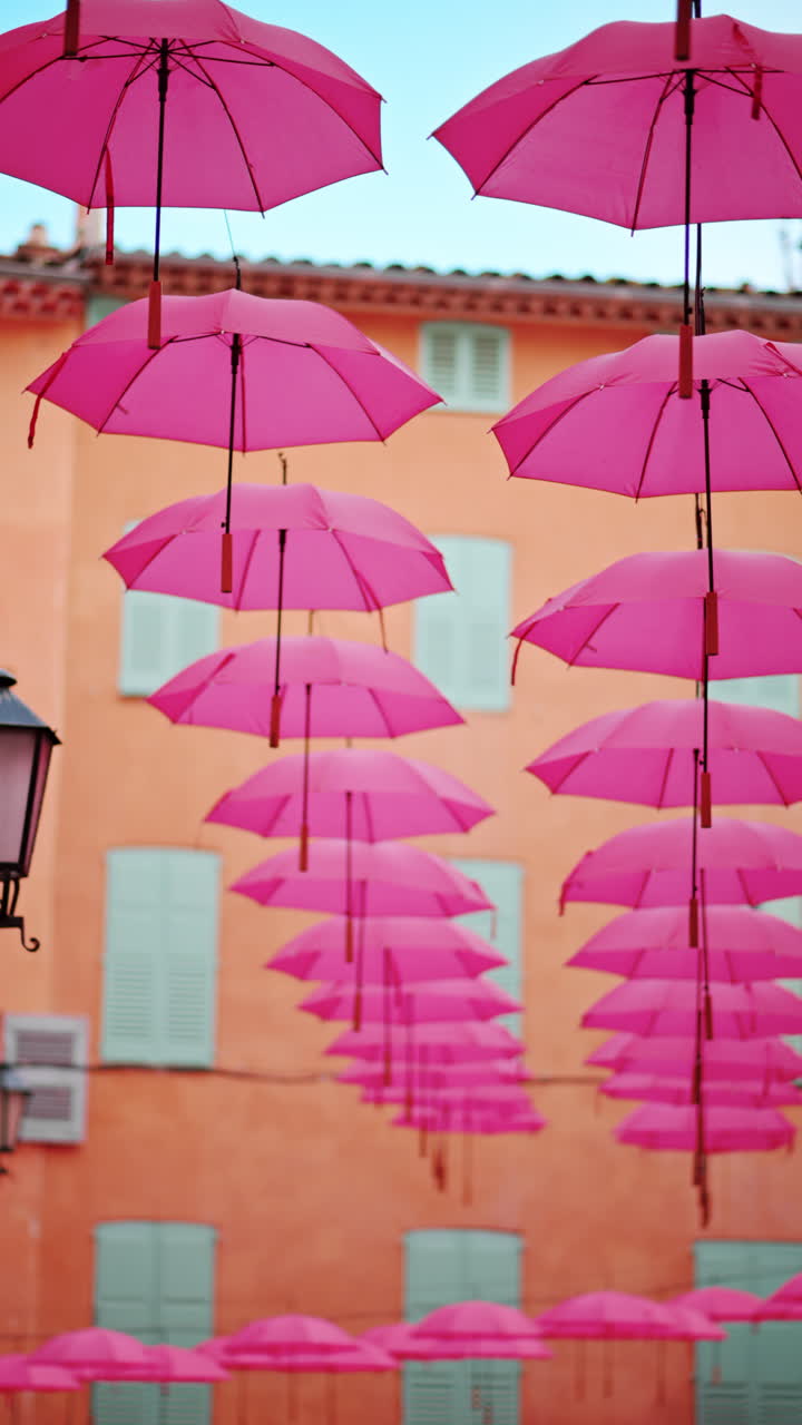Rows of pink umbrellas above the streets of the old town in Grasse, France. Vertical