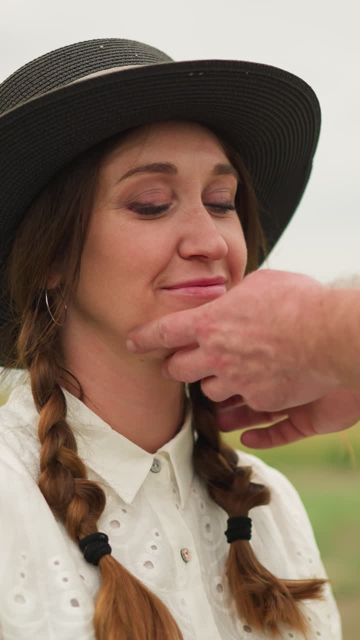 una escena encantadora donde una mujer con un vestido blanco y un sombrero negro se sienta en una silla en un campo sereno. sonríe tímidamente mientras la mano de un escultor ajusta suavemente su sombrero y su cabello