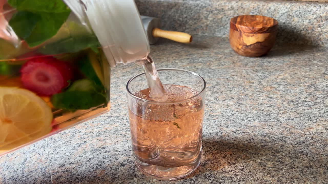 verter agua con infusión de frutas en un vaso en el mostrador de la cocina, primer plano