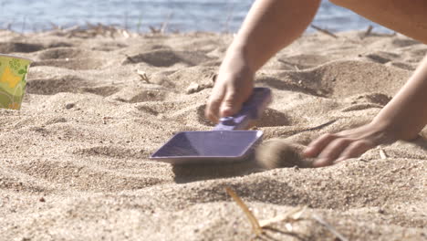 close-up of kid’s arms and legs as it plays with spade on sand beach