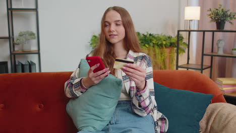 woman sitting at home using credit bank card and smartphone while transferring money online shopping