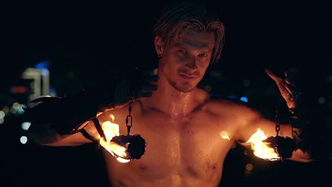 young blond male lifts two burning pois hanging on chains slow motion shot close-up