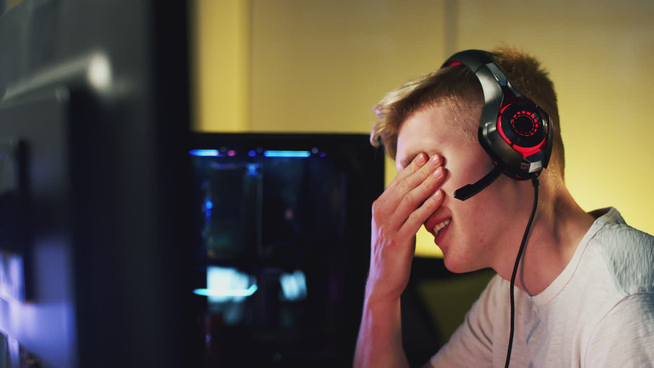 Excited Teenage Boy Wearing Headset Losing At Gaming At Home Using Dual Computer Screens