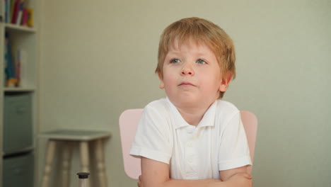 Small-schoolboy-listens-to-teacher-with-folded-hands-on-desk