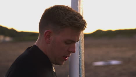 young man wearing wetsuit holding surfboard enjoying surfing vacation on beach as sun sets