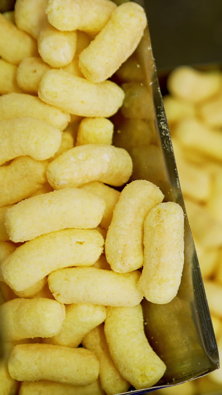 Production process of corn snacks at up-to-date food factory. Crunchy yellow sticks lifted by conveyor belt. Close up. Vertical video