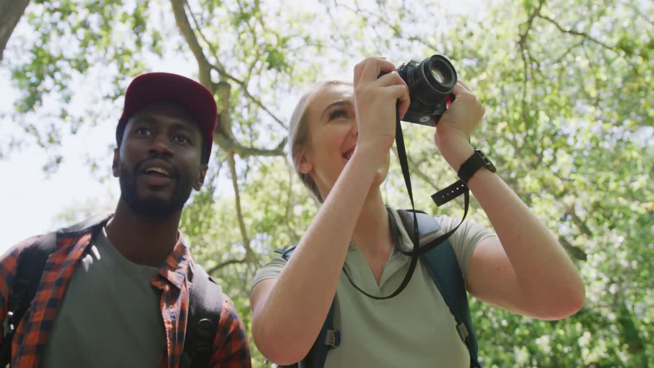 pareja feliz diversa con mochilas tomando fotos en el parque, cámara lenta