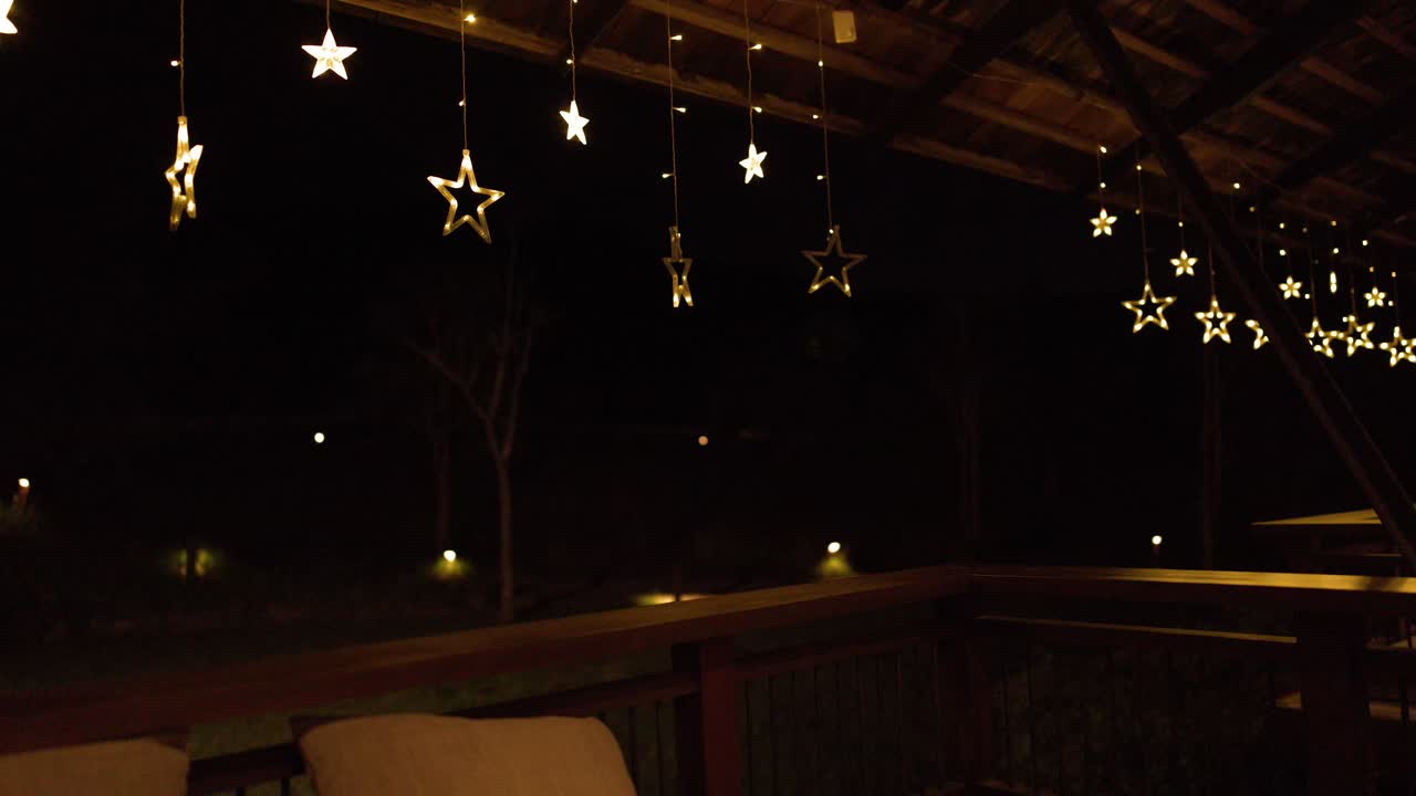 Warm star shaped string lights hang from a dark wooden terrace ceiling during nighttime