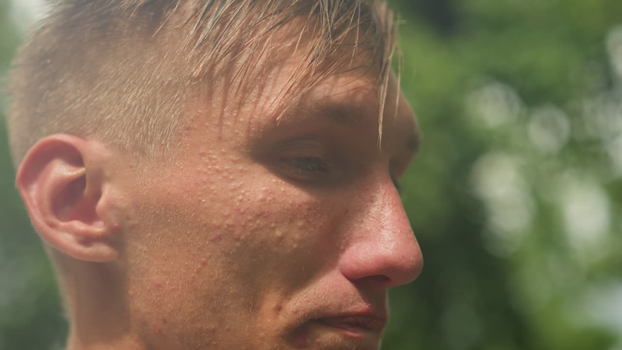 retrato de un hombre blanco bajo una ligera llovizna, actor haciendo una pausa entre frases, ojos cerrados y mano cerca de la boca, pelo mojado y piel brillante, bokeh de follaje verde, ambiente melancólico y nublado