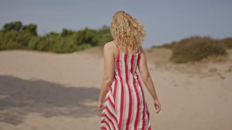 close-up of a woman's back as she walks across pale sand dunes on a sunny summer day in slow motion