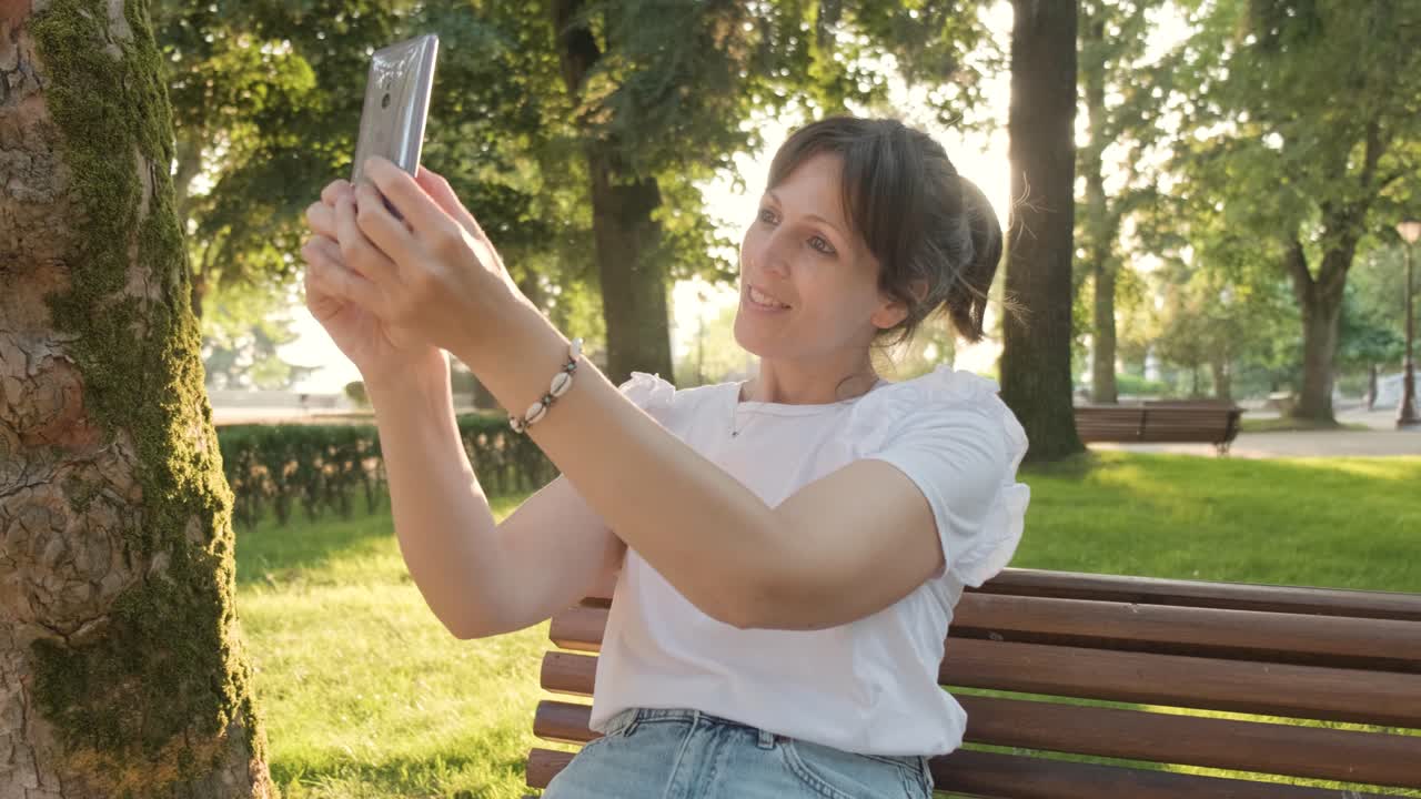 una mujer tomando una selfie con su teléfono mientras está sentada en el parque, toma de mano