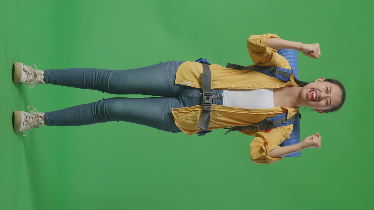 아시아 여성 하이커의 몸이 가득 차 있으며, 산악 배이 울부고 있으며, 스튜디오의 녹색 스크린 배경에 서서 성공을 축하하고 있습니다.