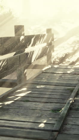 a wooden bridge in a misty forest with sunlight streaming through the trees