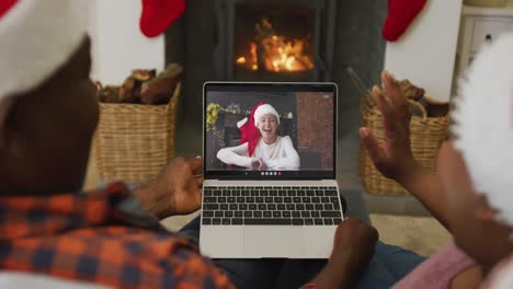 Afroamerikanisches-Paar-Mit-Weihnachtsmützen-Nutzt-Laptop-Für-Weihnachtsvideoanruf-Mit-Frau-Auf-Dem-Bildschirm