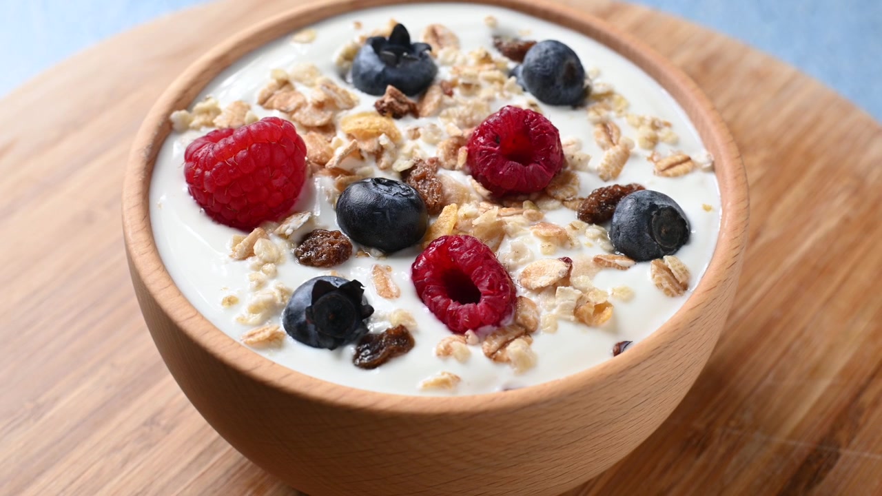 Yogurt con frutti di bosco e muesli per colazione in una ciotola che ruota su sfondo blu
