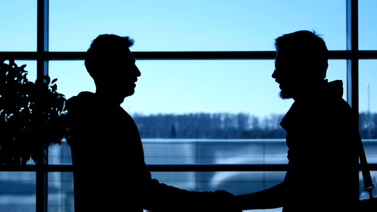 Silhouette of two man shaking hands and greeting in hall of business center