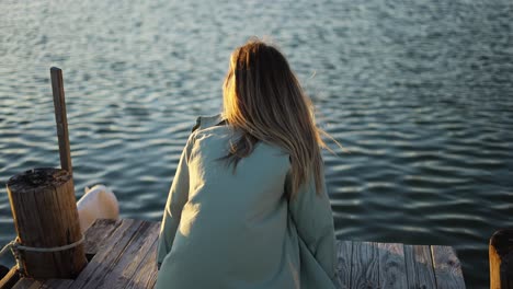 chica rubia sentada en un muelle de madera, vista de atrás