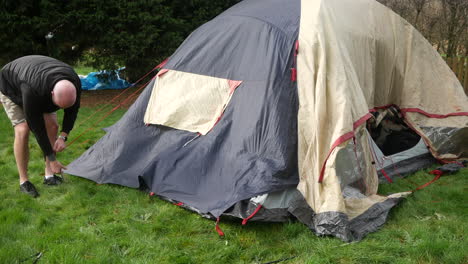 a man taking down a tent removing pegs after a camping trip