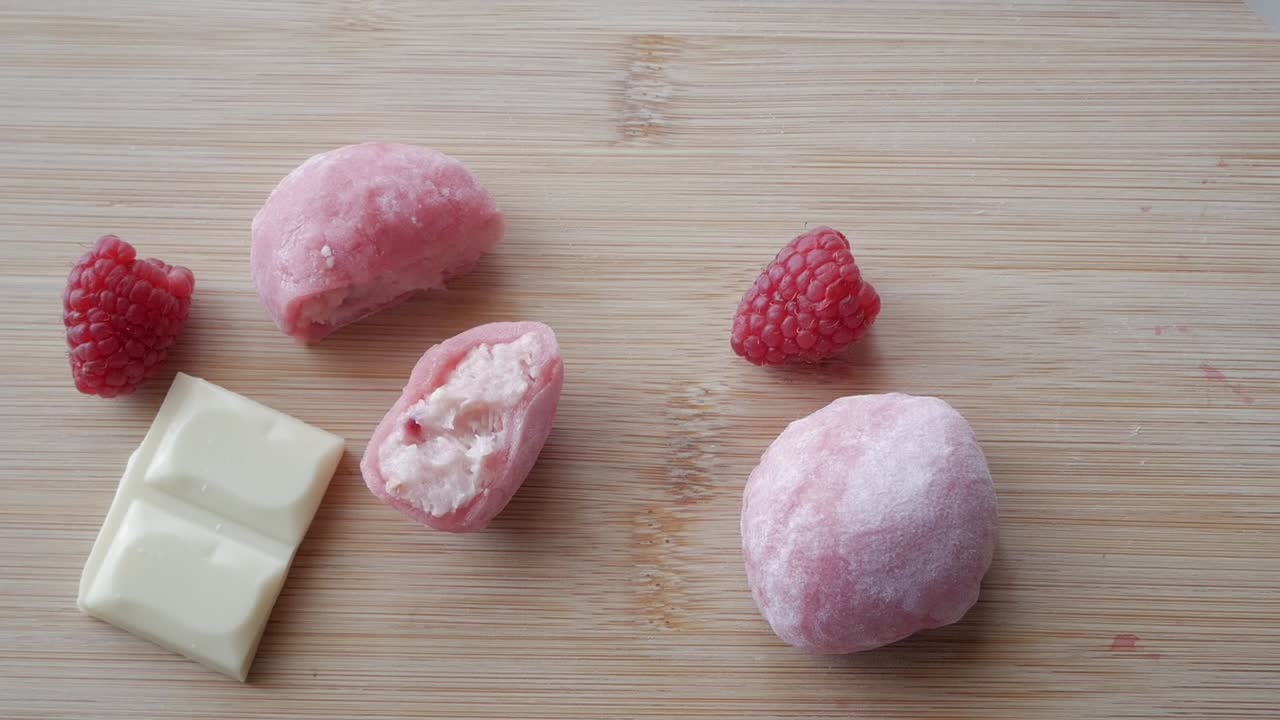 Sweet strawberry and white chocolate mochi on a wooden surface with raspberries